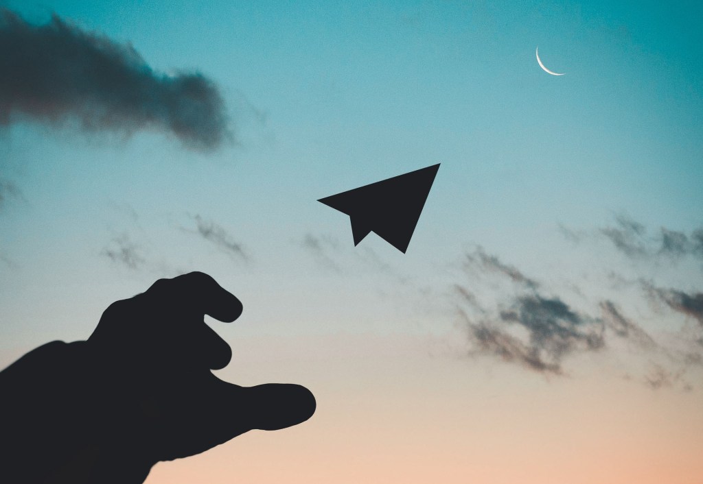 Silhouette photo of man throwing a paper plane in front of a sunset.