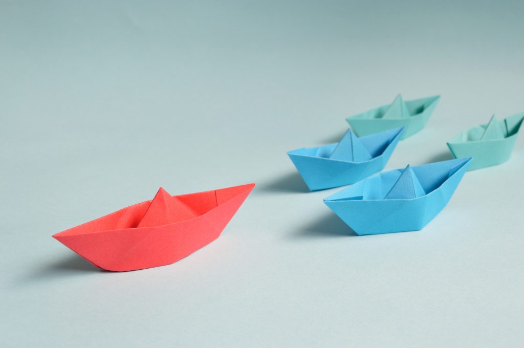 Red paper boat leader of small blue paper boats